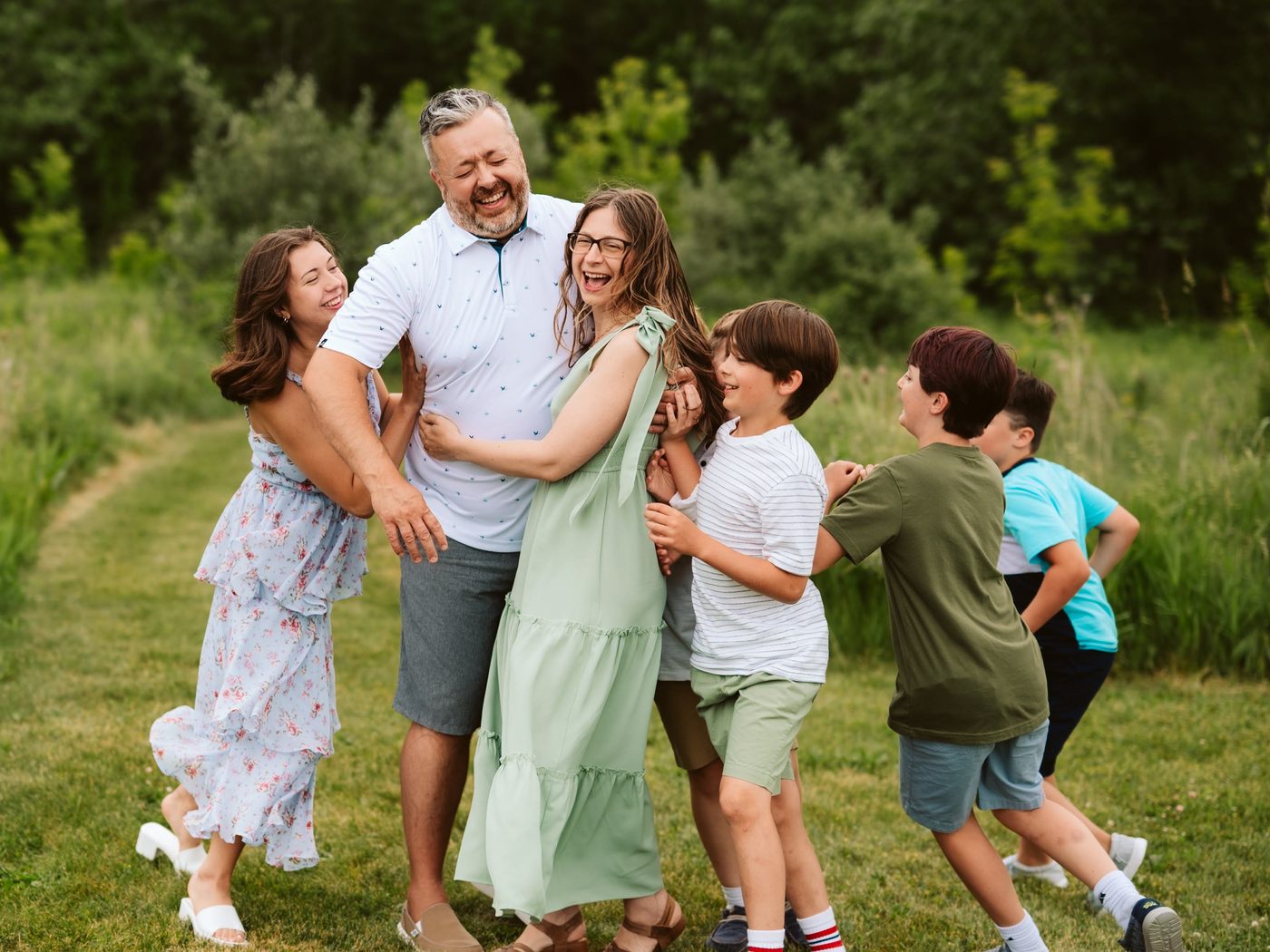 Justin, his wife, and their five kids laughing and piling into a group hug in a grassy field