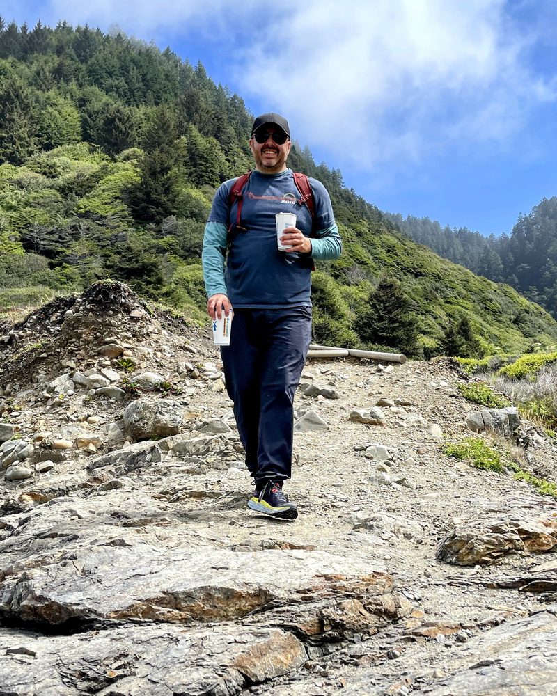 Justin hiking down a rocky trail, carrying two coffees